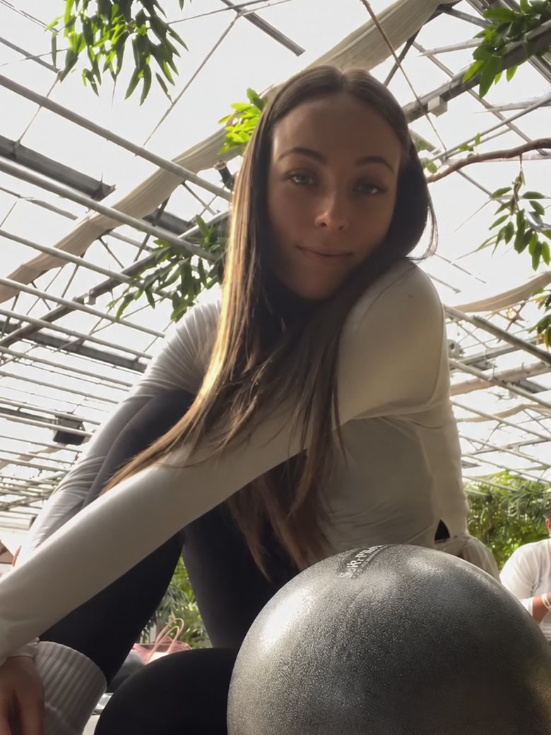 Tessi lacht mit einem Pilates-Ball in die Kamera
